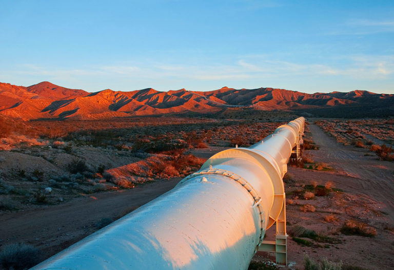 an oil pipeline in the red desert, off white and contrasting with the rolling red hills in the background