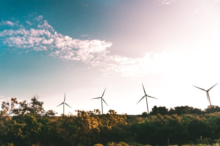 a sunny day with a smattering of clouds above a gentle forest topped by four wind turbines providing power
