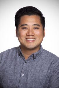 image of David Lee wearing a gray shirt and smiling at the camera against a white background.